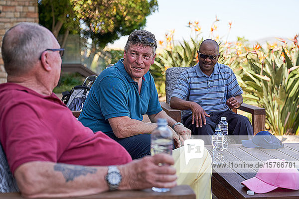 Ältere männliche Golffreunde unterhalten sich und trinken Wasser auf der Terrasse