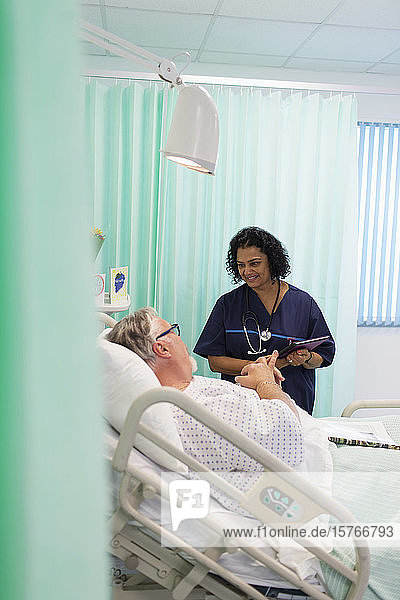 Arzt mit digitalem Tablet bei der Visite  Gespräch mit älterem Patienten im Krankenhauszimmer