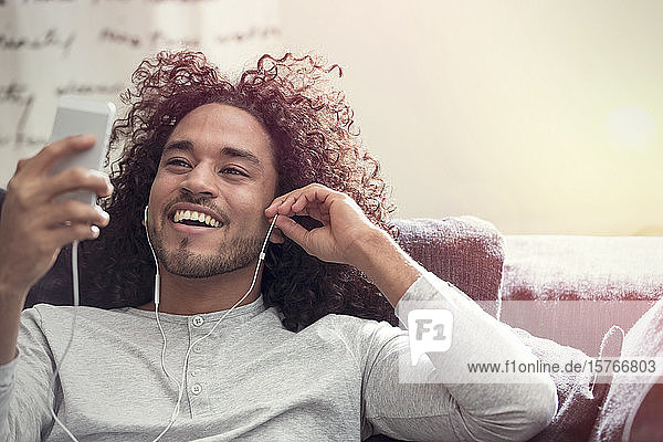 Lächelnder junger Mann  der mit Kopfhörern und mp3-Player Musik hört