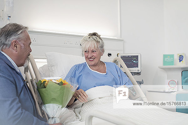 Älterer Mann mit Blumenstrauß besucht Frau im Krankenhaus