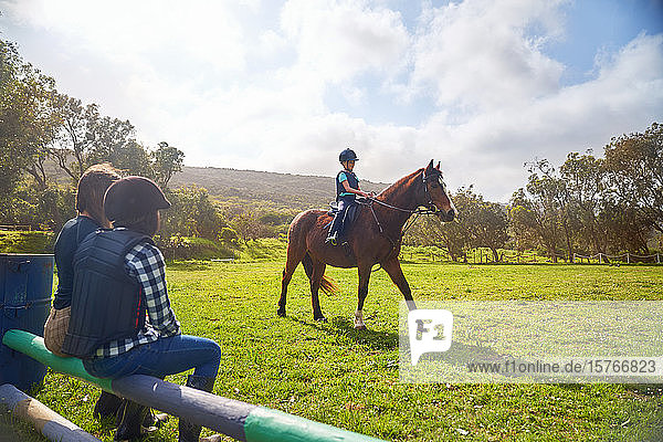Girl horseback riding in sunny grass paddock
