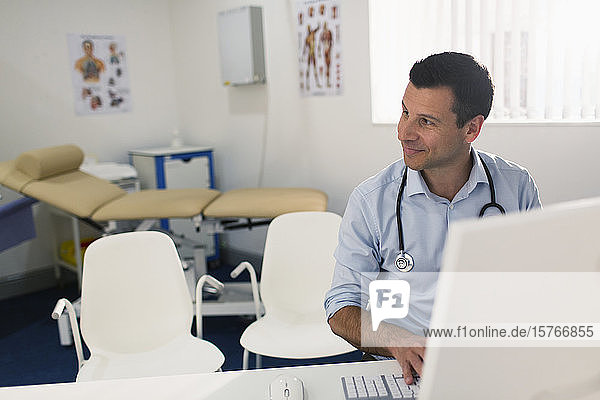 Confident male doctor working at computer in doctors office