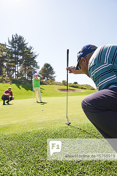 Männlicher Golfer bereitet sich auf einen Schlag auf dem sonnigen Putting Green vor