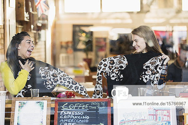 Glückliche junge Freundinnen mit passenden Pullovern im Schaufenster eines Cafés