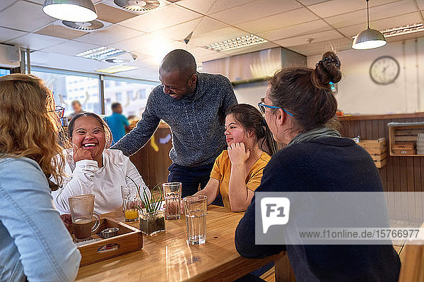 Glückliche junge Frau mit Down-Syndrom im Café mit Freunden
