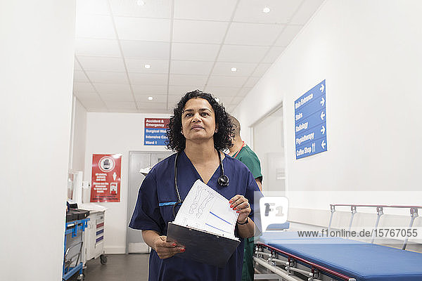 Confident female doctor with medical chart making rounds in hospital corridor