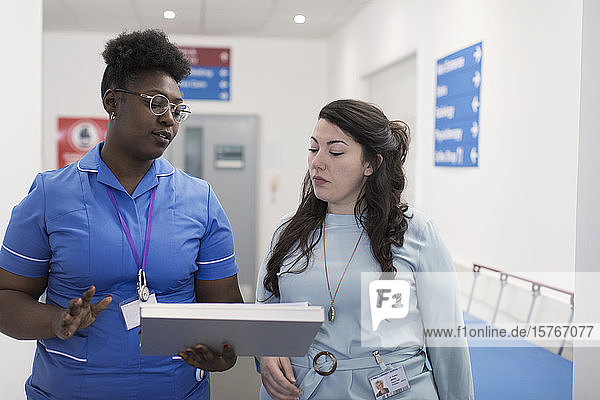 Female doctor and nurse making rounds  discussing medical chart in hospital corridor