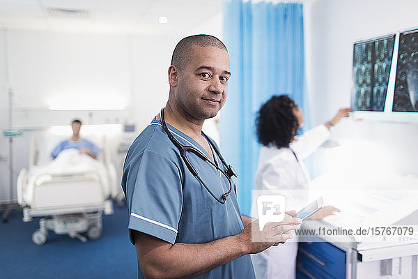 Porträt eines selbstbewussten  lächelnden Arztes  der ein digitales Tablet in einem Krankenhauszimmer benutzt