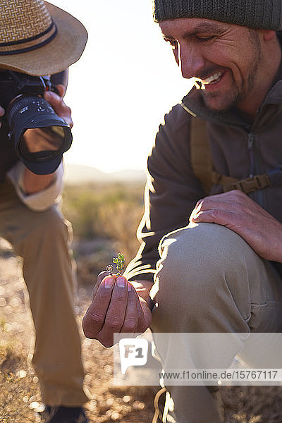 Lächelnder Safari-Reiseleiter erklärt einem Mann mit Digitalkamera die Pflanze