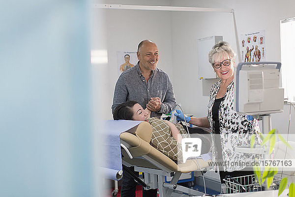 Techniker bei der Durchführung von Ultraschalluntersuchungen für ein glückliches schwangeres Paar im Untersuchungsraum