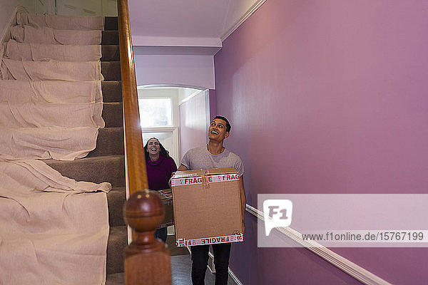 Glückliches Paar zieht in ein neues Haus ein und trägt Kartons durch den Flur
