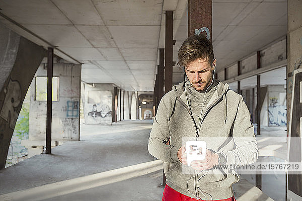 Junger männlicher Läufer hört Musik mit mp3-Player und Kopfhörern in einem verlassenen Gebäude