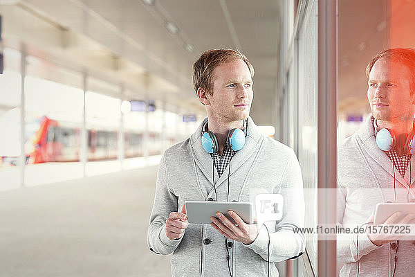 Junger Mann mit digitalem Tablet und Kopfhörern wartet in der Nähe des Bahnsteigs