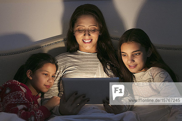 Mutter und Töchter benutzen ein digitales Tablet in einem dunklen Schlafzimmer