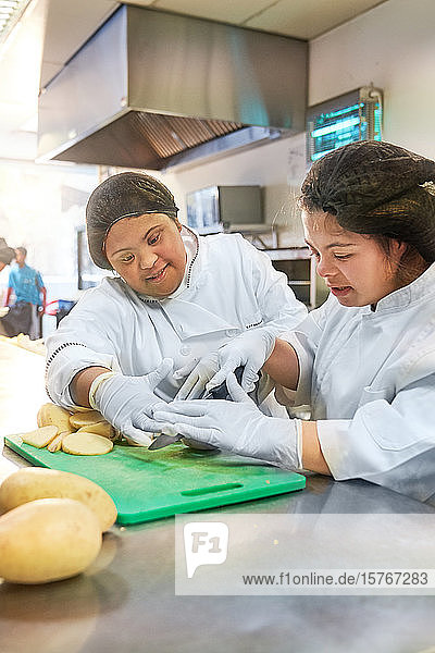 Junge Frauen mit Down-Syndrom schneiden Kartoffeln in der Küche eines Cafés