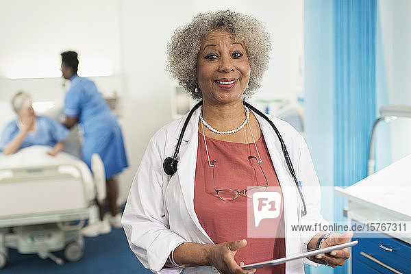 Porträt einer selbstbewussten Ärztin  die ein digitales Tablet in einem Krankenhauszimmer benutzt