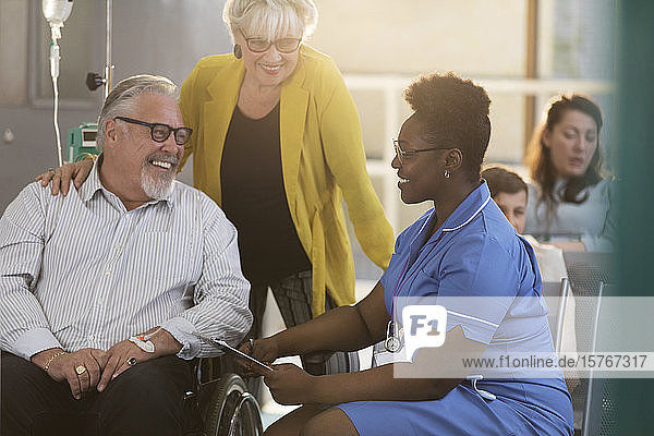 Weibliche Krankenschwester im Gespräch mit einem älteren männlichen Patienten im Rollstuhl in der Kliniklobby