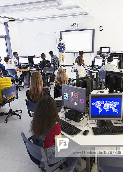 Schüler der Mittelstufe an Computern hören dem Lehrer auf der Projektionsfläche im Klassenzimmer zu