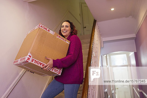 Porträt einer lächelnden Frau  die umzieht und einen Karton auf einer Treppe trägt