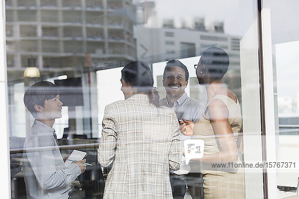 Lächelnde Geschäftsleute im Gespräch am sonnigen Bürofenster