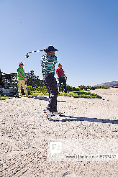 Männlicher Golfer bei einem Schlag aus einem sonnigen Golfbunker