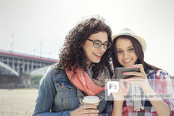 Junge Frauen  die ein Smartphone benutzen und im Freien Kaffee trinken