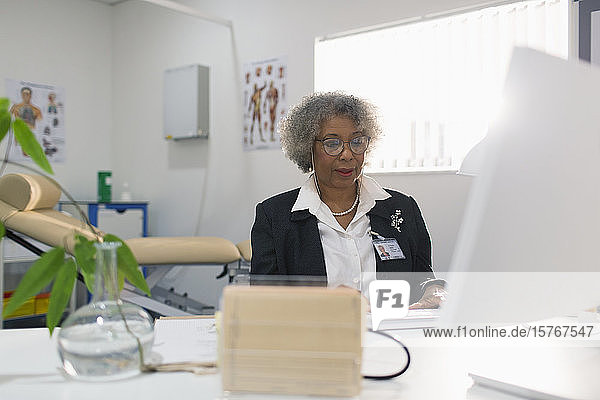 Female senior doctor working at computer in doctors office