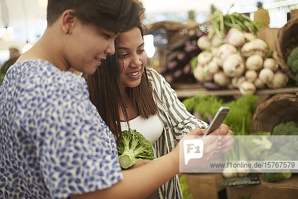 Lesbisches Paar mit Smartphone beim Einkaufen auf dem Bauernmarkt