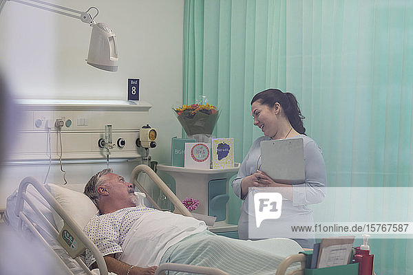 Arzt mit Krankenblatt im Gespräch mit älterem Patienten im Krankenhauszimmer