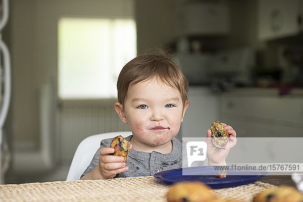 Portrait cute toddler girl eating messy muffin