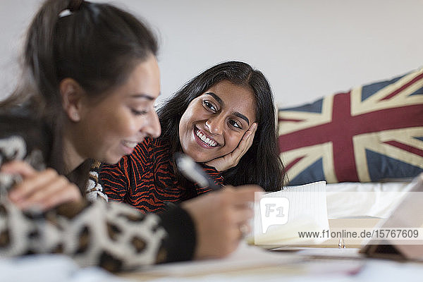Lächelnde Teenager-Freundinnen  die auf dem Bett Hausaufgaben machen