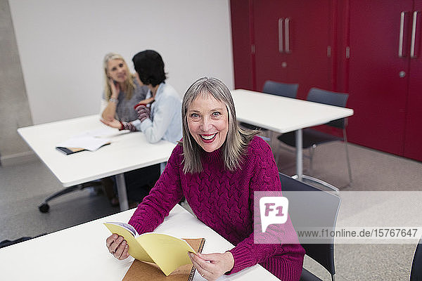 Porträt einer lächelnden  selbstbewussten Studentin einer Volkshochschule  die im Klassenzimmer liest