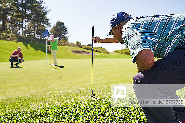 Male golfer preparing to putt on sunny golf course