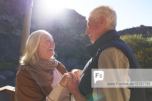Glückliches älteres Paar hält sich auf einem sonnigen Balkon an den Händen