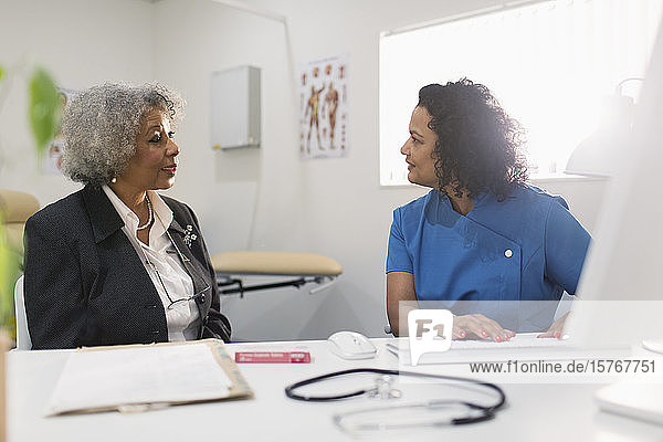 Female doctor talking with senior patient at computer in doctors office