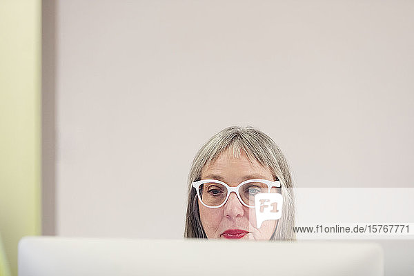 Fokussierte reife Frau mit Brille am Computer