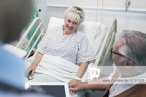 Zärtlicher älterer Mann im Gespräch mit seiner im Krankenhausbett liegenden Frau