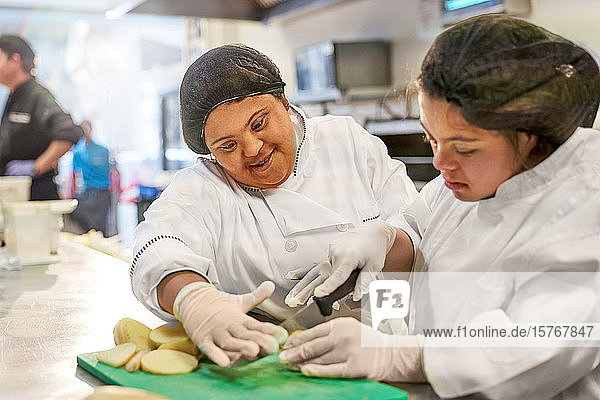 Lächelnde junge Frau mit Down-Syndrom beim Kartoffelschneiden in der Küche