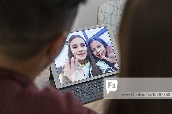 Daughters on digital tablet waving to parents  video conferencing with parents
