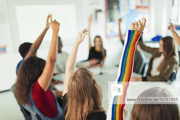 Gymnasiasten mit erhobenen Armen  die im Klassenzimmer Fragen stellen