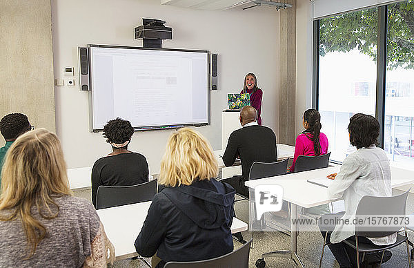 Female community college instructor leading lesson at projection screen in classroom
