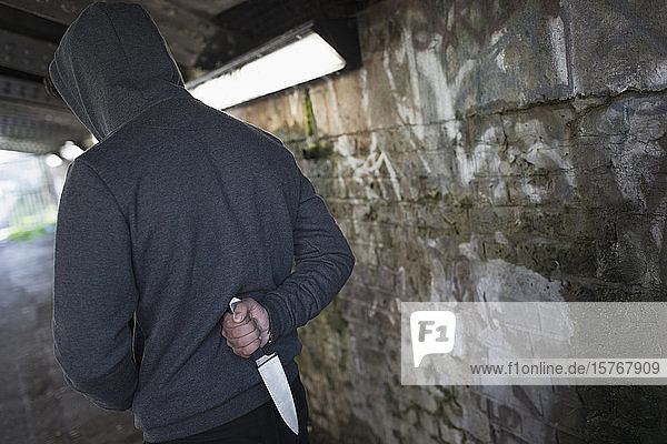 Gefährlicher Mann mit Messer im Rücken in städtischem Tunnel