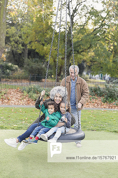 Großeltern und Enkelkinder spielen auf einer Reifenschaukel im Park