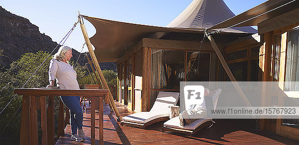 Sorgloses älteres Paar entspannt sich auf dem sonnigen Balkon einer Luxus-Safari-Lodge