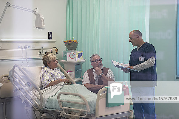 Arzt mit Krankenblatt im Gespräch mit einem älteren Ehepaar im Krankenhauszimmer