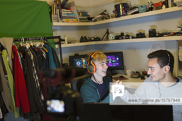 Happy teenage boys with headsets playing video game at computer in bedroom