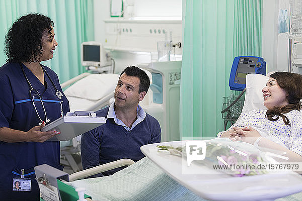 Arzt mit Krankenblatt bei der Visite  Gespräch mit Paar im Krankenhauszimmer