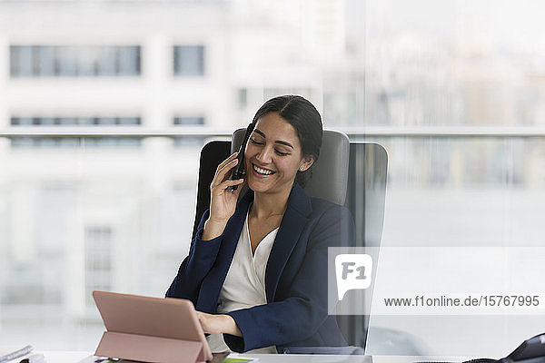 Lächelnde Geschäftsfrau  die im Büro mit einem Smartphone telefoniert