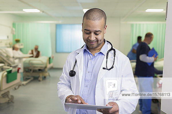 Smiling male doctor with digital tablet making rounds in hospital ward