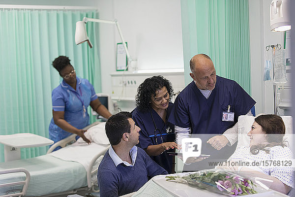 Ärzte mit digitalem Tablet bei der Visite und im Gespräch mit Patienten auf der Krankenstation